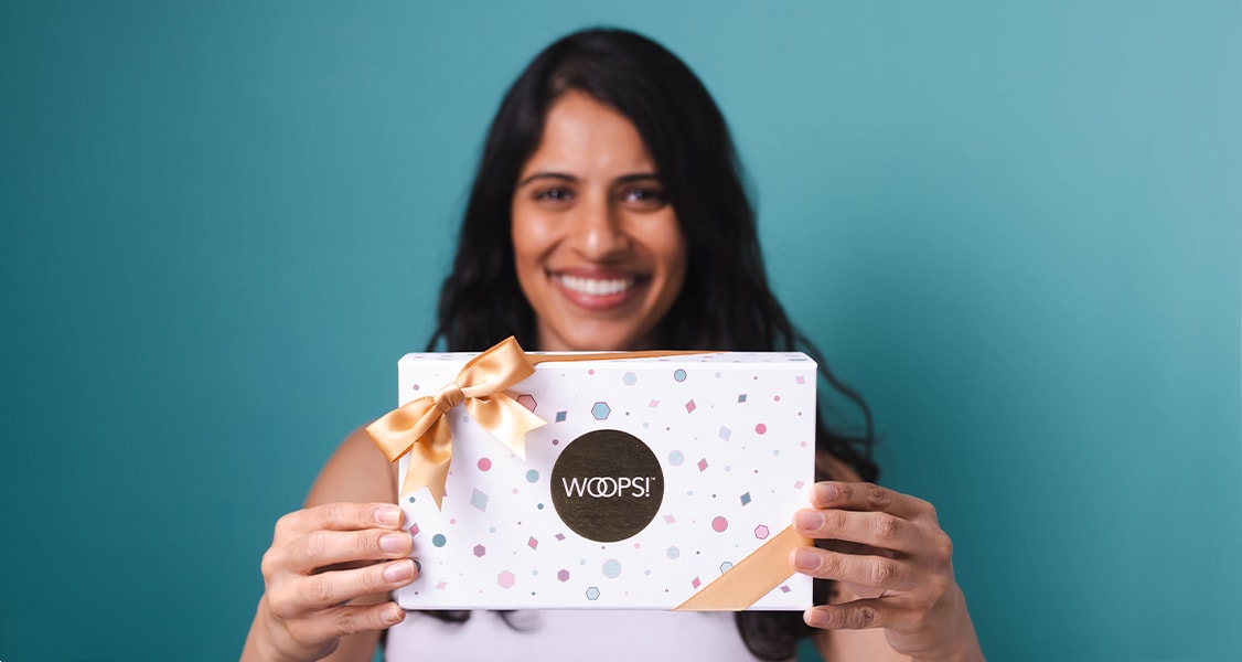 A smiling woman is holding a white Woops! box of 9 French macarons.