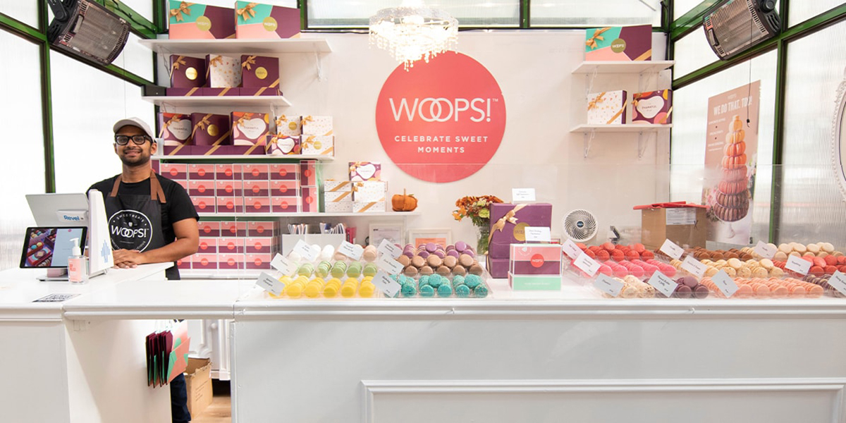 An employee of a Woops! French macaron franchise kiosk stands at the register.