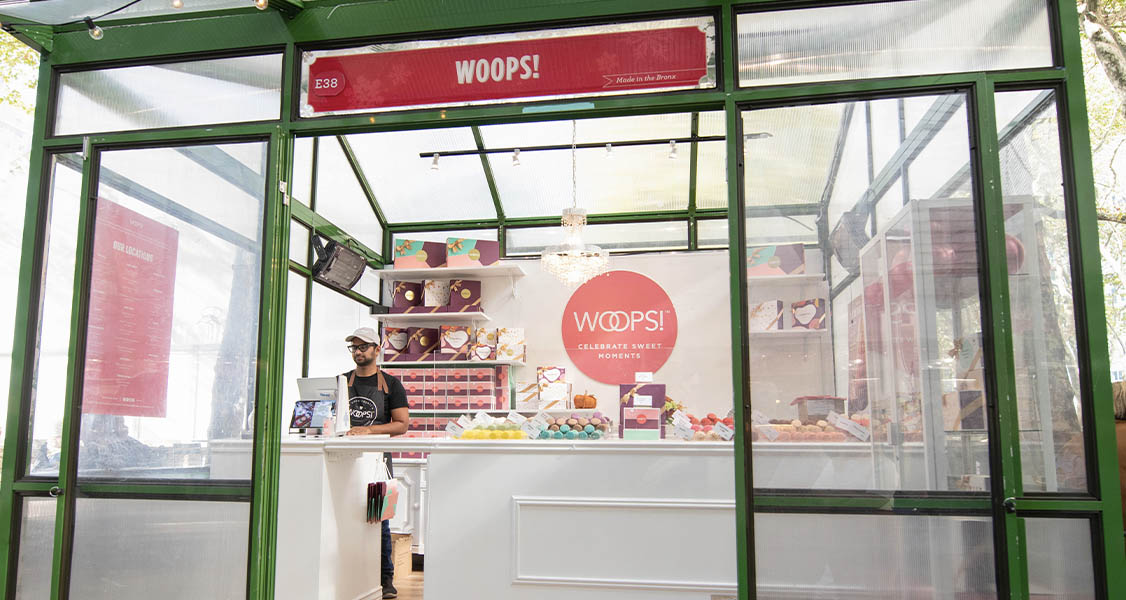 A Woops! Macarons & Gifts green pop-up shop. Inside is a counter full of assorted macarons and macaron boxes. 