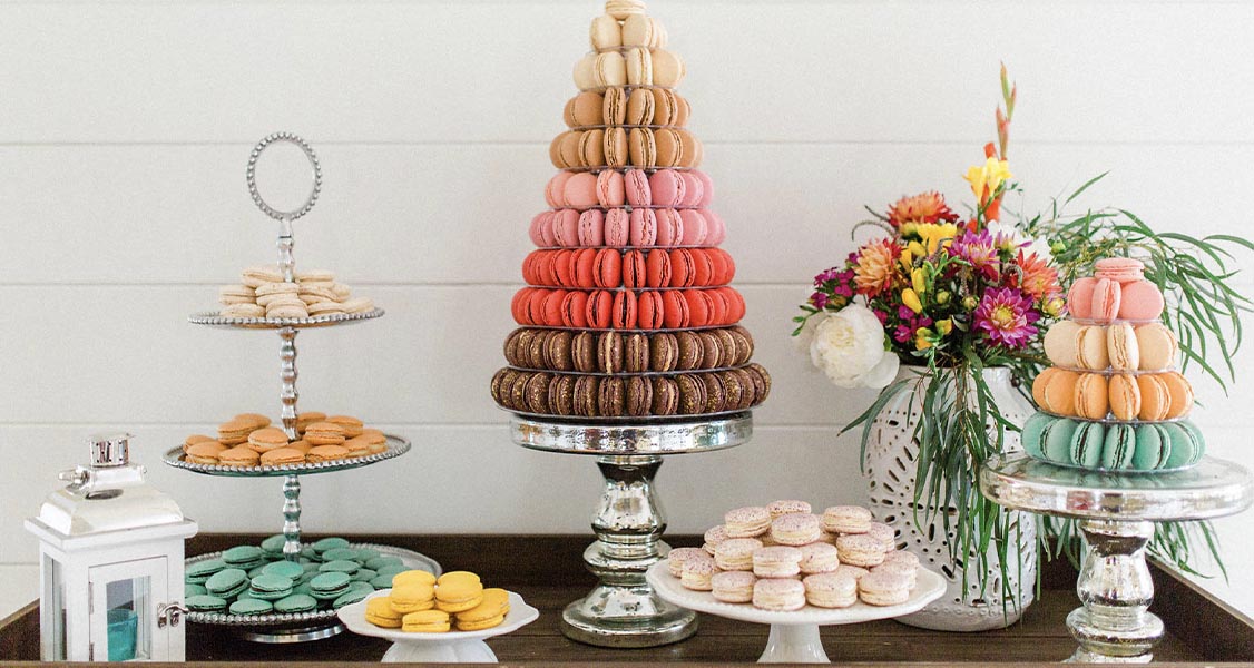 A table is full of macaron treats, including two macaron towers, plates of macarons, and a three-tier serving tray full of macarons. Woops! is a top macaron franchise.