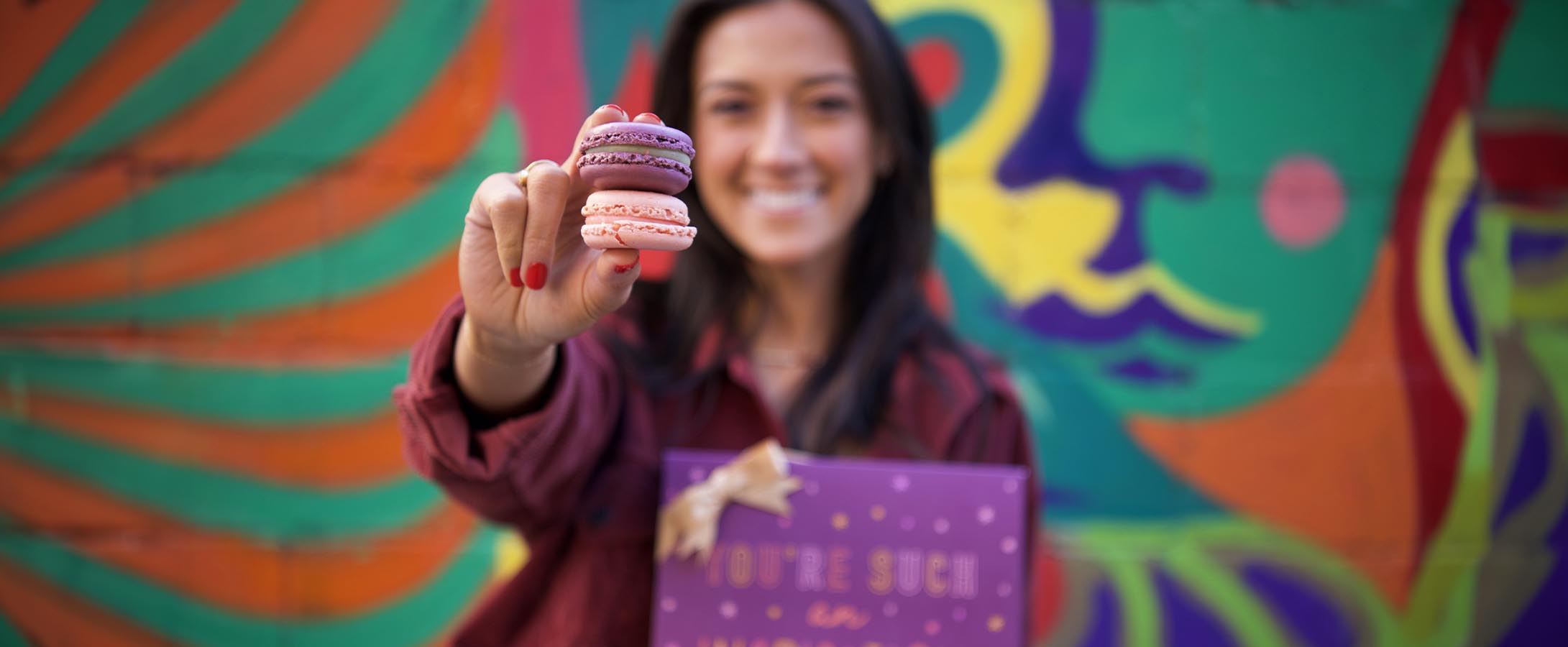 A smiling girl holds out two macarons in her fingers. Owning a Woops! is a great way to make a positive impact in your community.