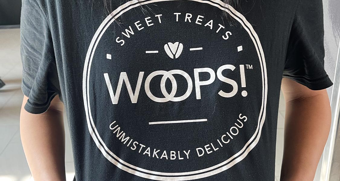 A woman with a Woops! Sweet Treats & Unmistakably Delicious black T-shirt.