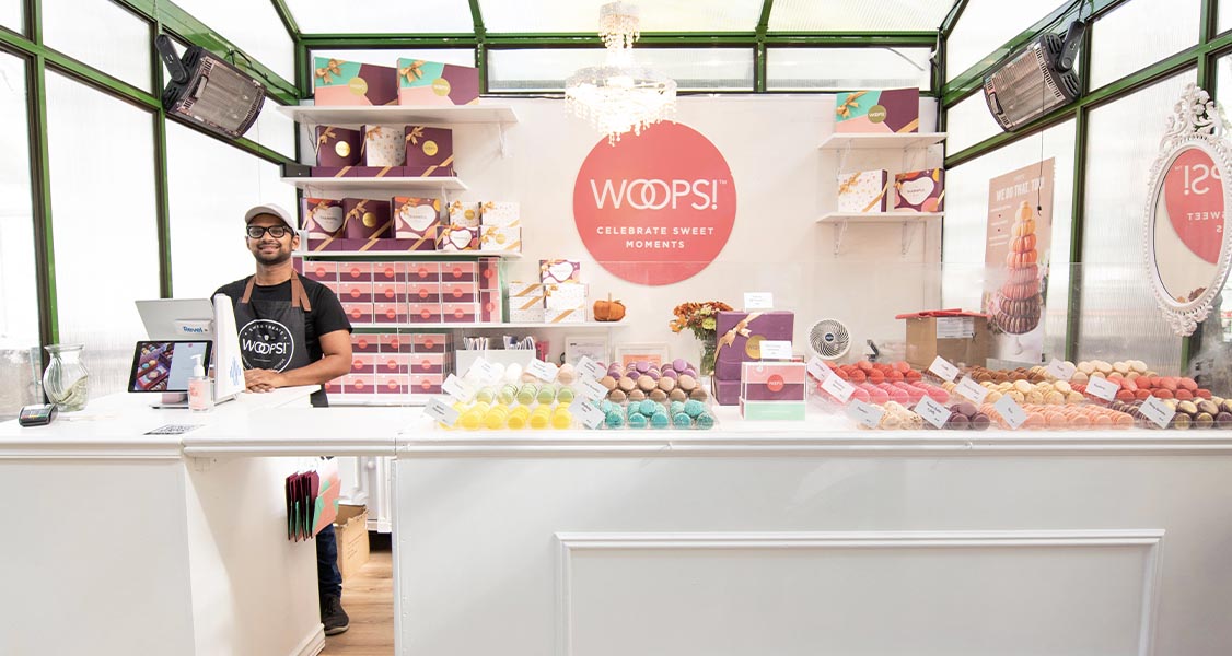 A Woops! Macarons & Gifts pop-up shop with a full display of macarons and macaron boxes. 