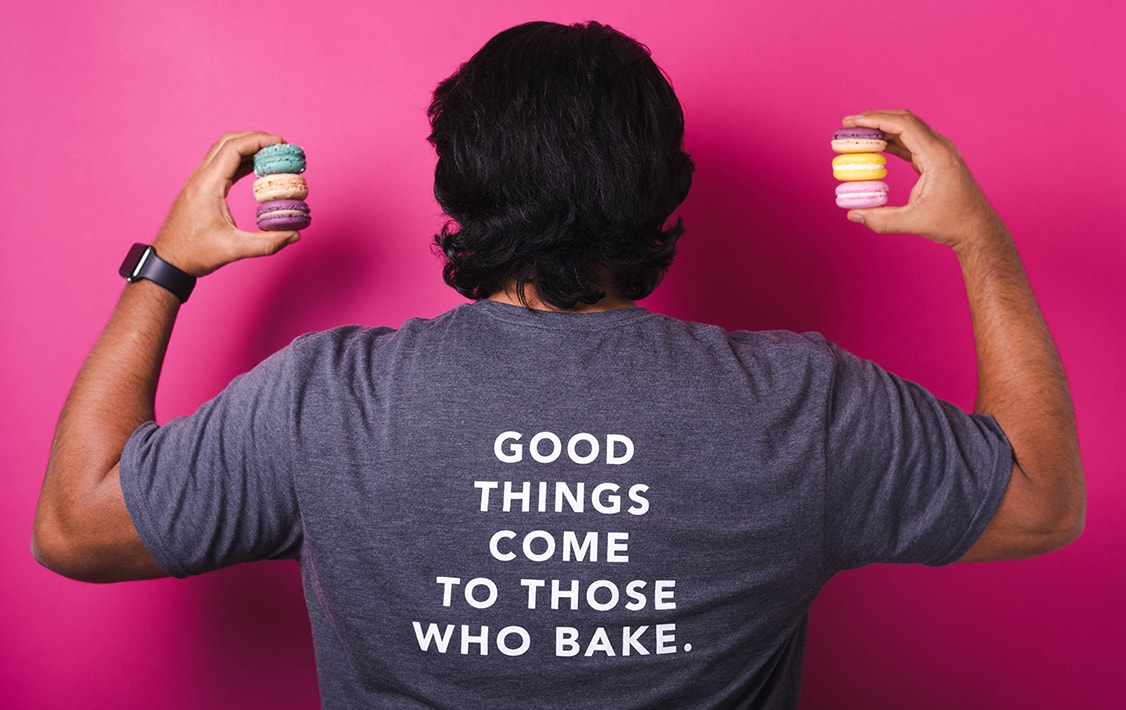 A man with a “Good Things Come To Those Who Bake.” t-shirt is holding macarons in his hands.