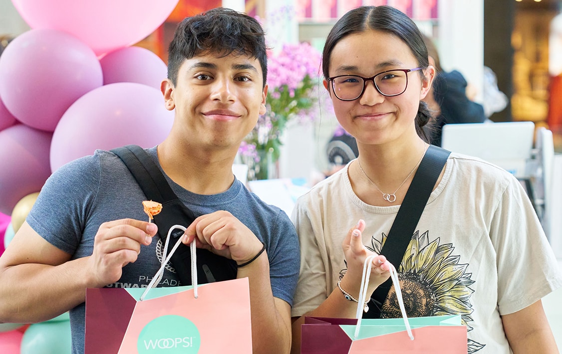 A smiling boy and girl holding Woops! Macarons & Gifts bags.