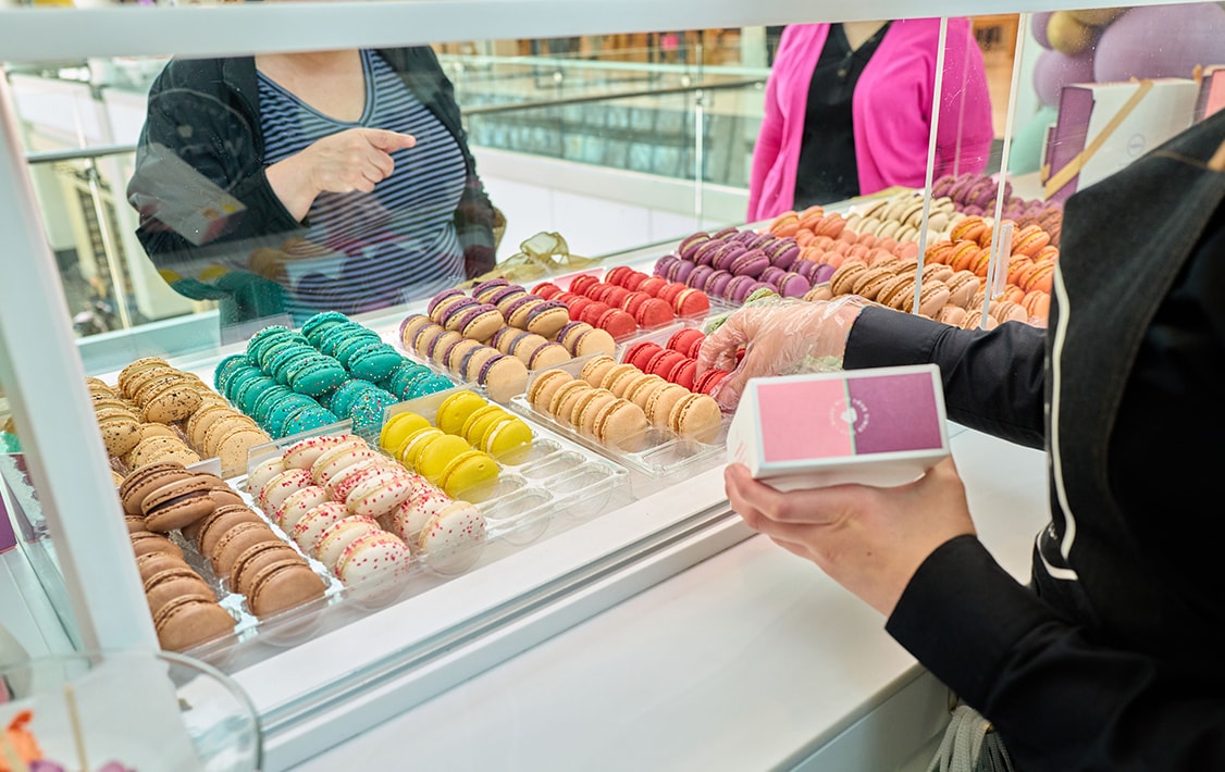 A big macaron showcase and a woman filling a box with macarons.