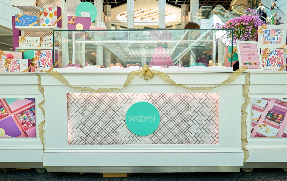 A Woops! Macarons & Gifts kiosk full of assorted macaron, macaron boxes, and inauguration decorations.