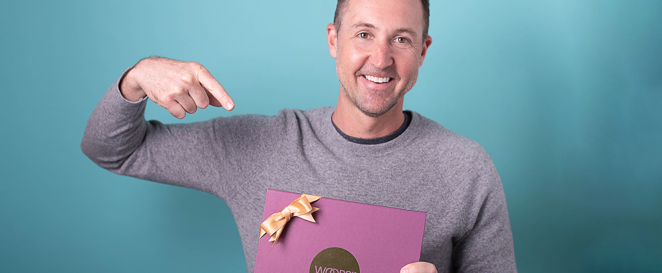 A smiling man holding a Woops! Purple macaron box and signaling it with his other hand.