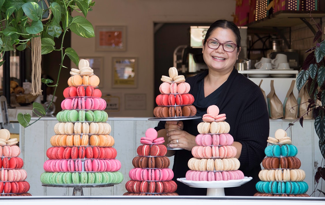 Smiling woman with several French macaron pyramids in front of her.