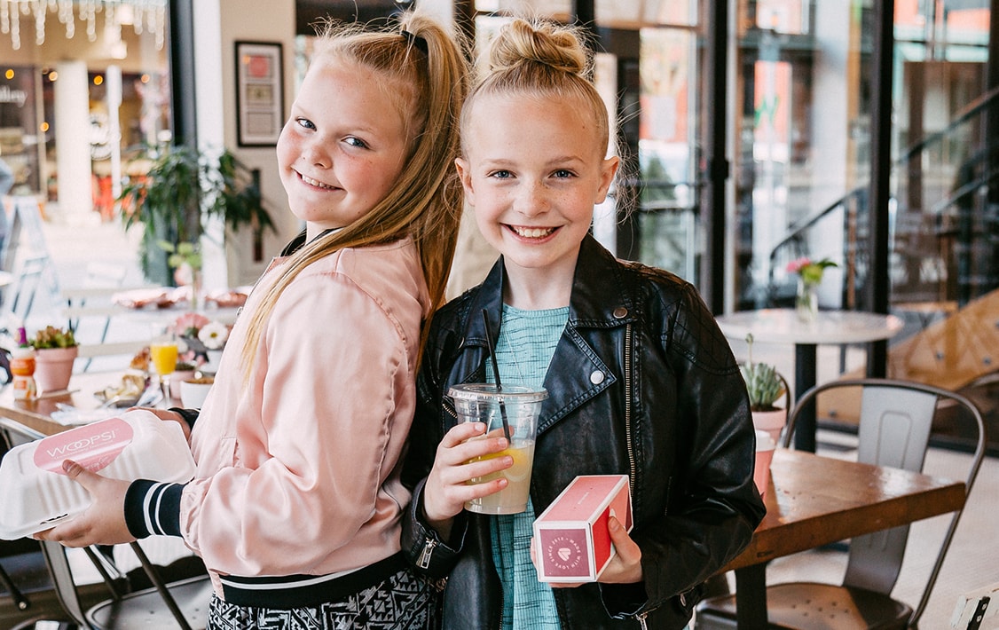 Two smiling girls holding French macaron boxes in their hands.