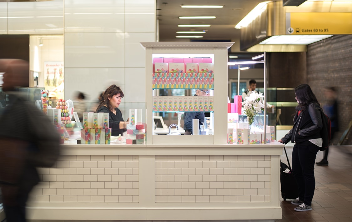 Woops! Macarons & Gifts kiosk with bustling people surrounding it. 