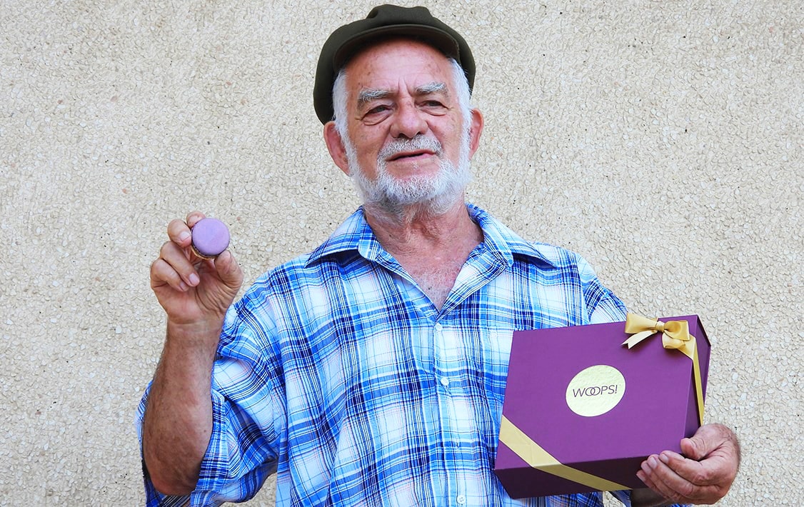 A man holding a macaron in one hand and a macaron box in the other.