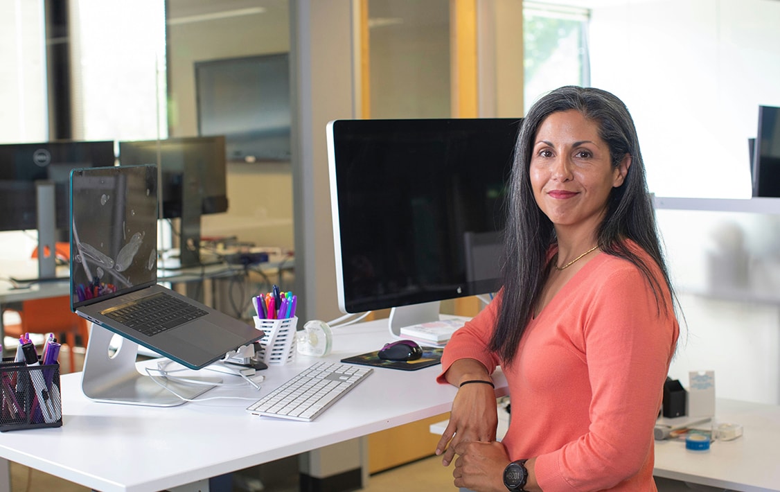 A smiling woman behind a desk full of computers and office supplies