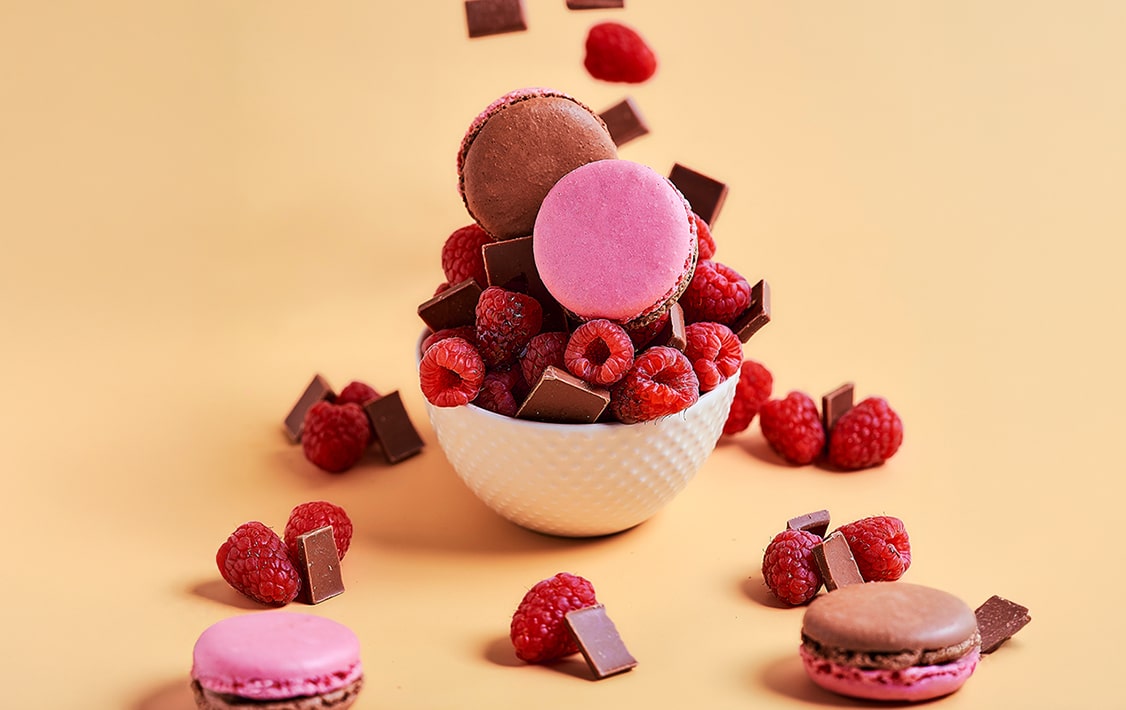 A cup of raspberries, chocolates and pink and brown Woops! macarons   