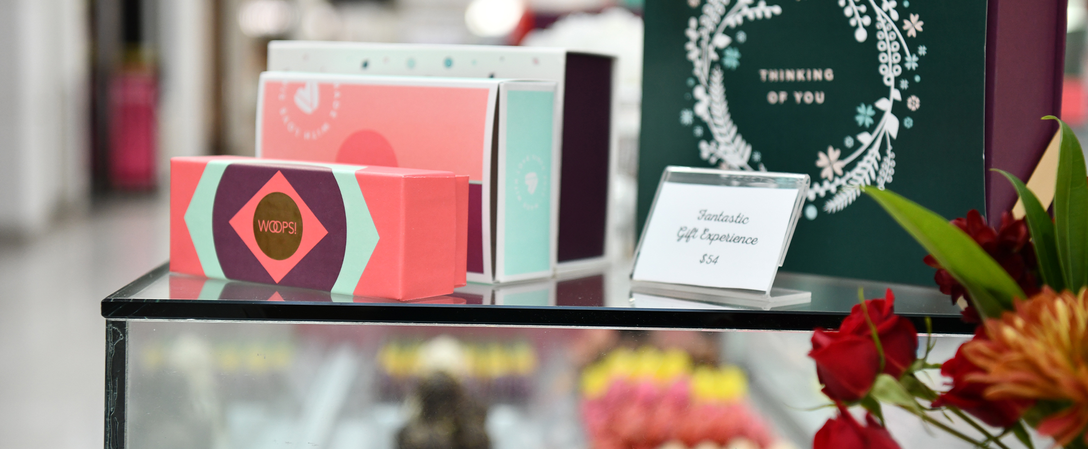Colorful Woops! macaron gift boxes displayed on top of a glass case with blurred macarons underneath.